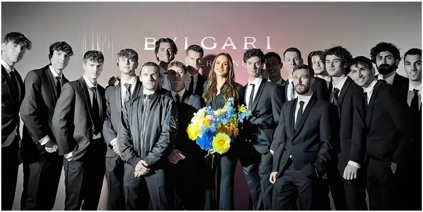 Hostess e staff di Hostess World Milano all’evento Bvlgari: gruppo di ospiti in abito nero formale, uno dei quali con un mazzo di fiori blu e gialli